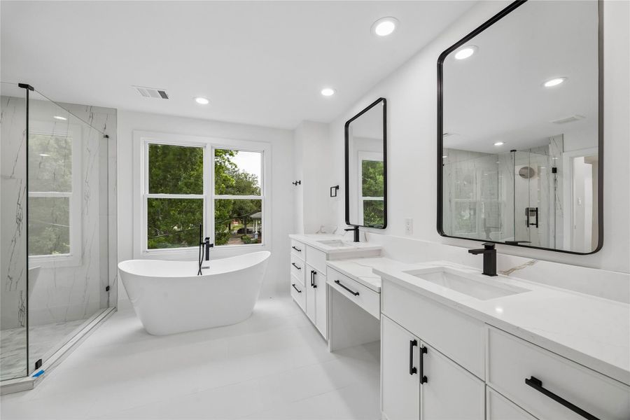 Modern vanity design, expansive counter space, layered lighting, and oversized framed mirrors create a polished primary bath environment designed for both functionality and everyday comfort. The neutral palette and clean-lined finishes continue the home’s contemporary aesthetic while maintaining warmth throughout the space.