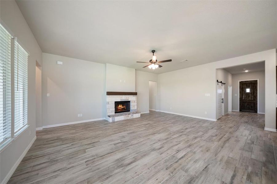 Unfurnished living room featuring a barn door, light wood-type flooring, a ceiling fan, and a fireplace Unfurnished living room featuring a barn door, light wood-type flooring, a ceiling fan, and a fireplace