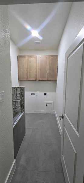 Laundry room featuring washer hookup, cabinet space, a textured wall, dark tile patterned flooring, and hookup for an electric dryer Laundry room featuring washer hookup, cabinet space, a textured wall, dark tile patterned flooring, and hookup for an electric dryer