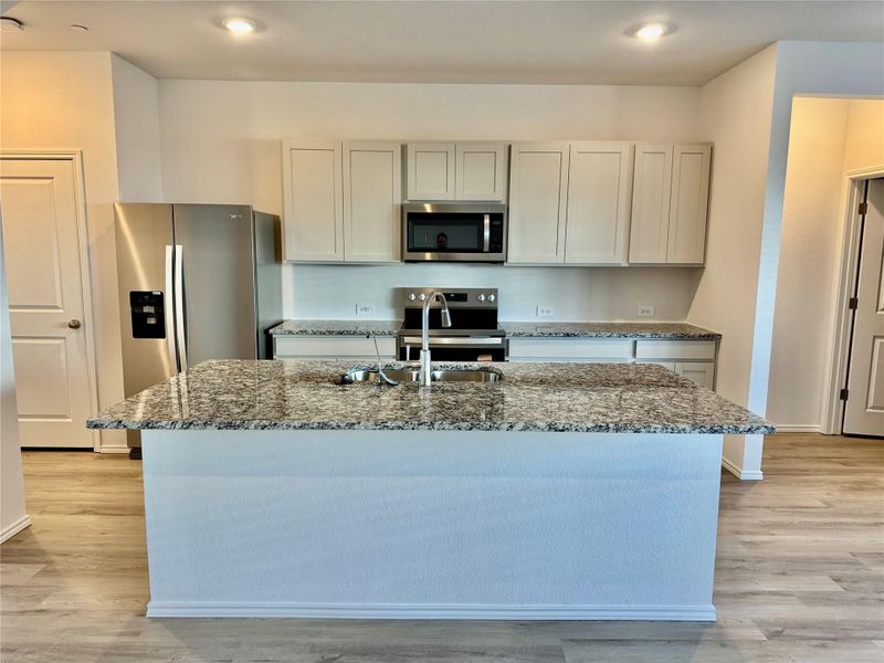 Kitchen featuring light stone countertops, stainless steel appliances, a kitchen island with sink, light wood-type flooring, and gray cabinets