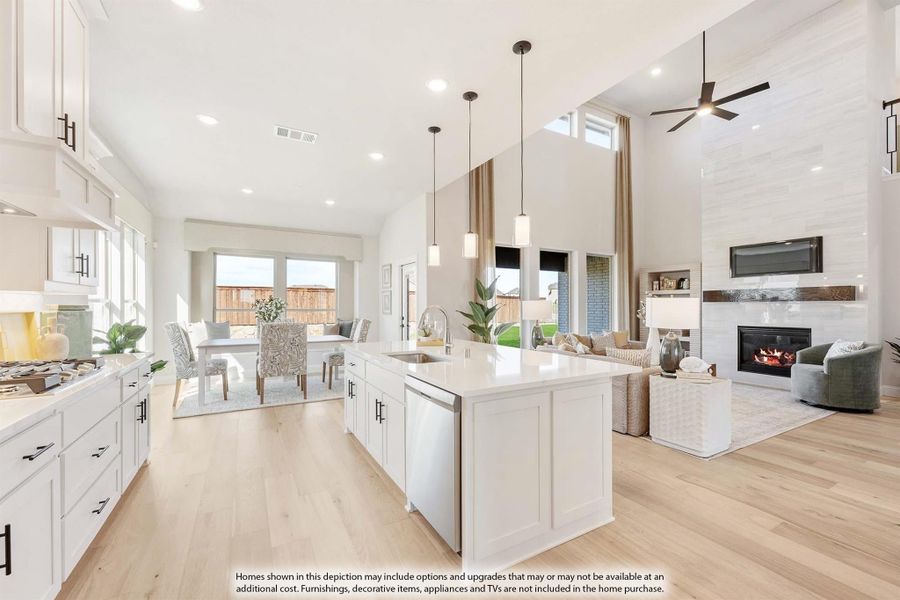 Open-concept kitchen with white island and cabinets, flowing into dining and living areas with fireplace and high ceilings