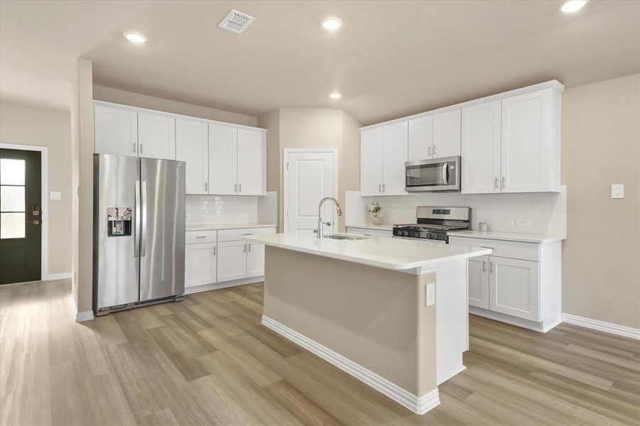 Kitchen featuring appliances with stainless steel finishes, white cabinetry, a kitchen island with sink, light wood-style flooring, and recessed lighting Kitchen featuring appliances with stainless steel finishes, white cabinetry, a kitchen island with sink, light wood-style flooring, and recessed lighting