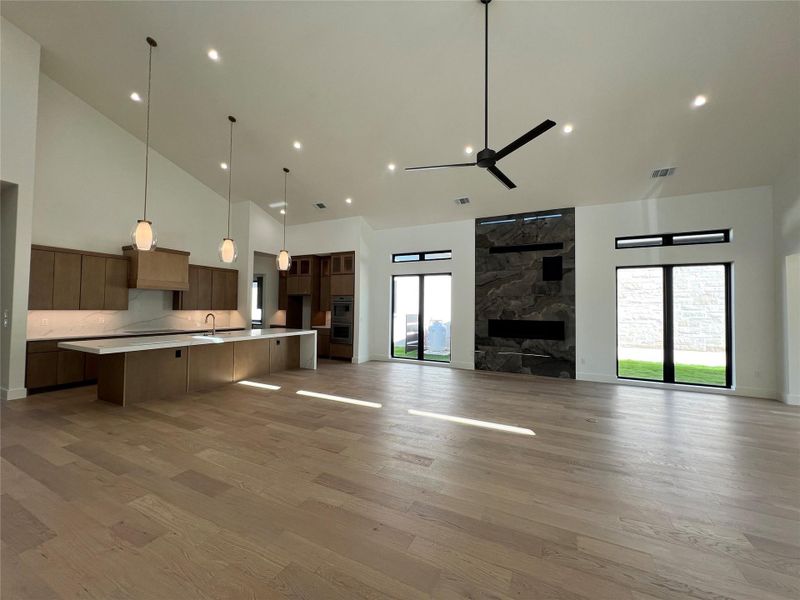 Unfurnished living room with ceiling fan, wood finished floors, vaulted ceiling, a fireplace, and recessed lighting