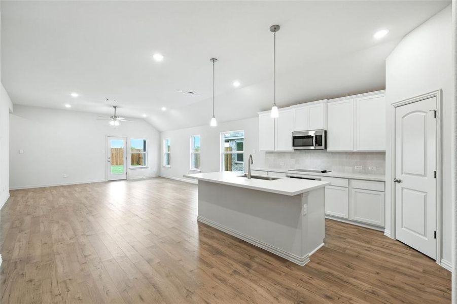 Kitchen with tasteful backsplash, vaulted ceiling, pendant lighting, white cabinetry, and recessed lighting Kitchen with tasteful backsplash, vaulted ceiling, pendant lighting, white cabinetry, and recessed lighting