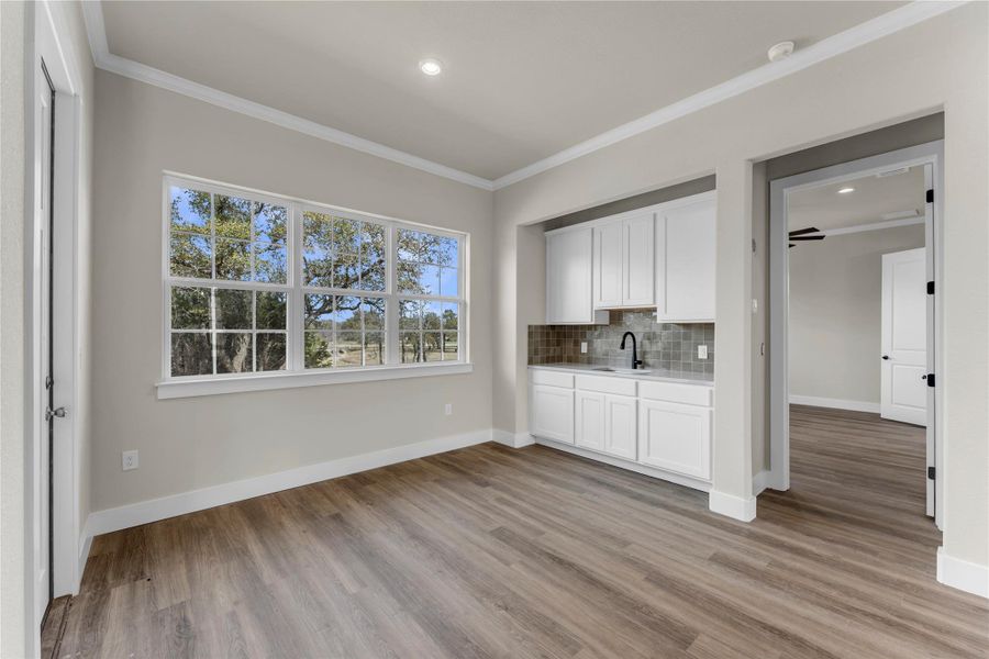 Bar area with crown molding, white cabinets, light countertops, light wood finished floors, and tasteful backsplash