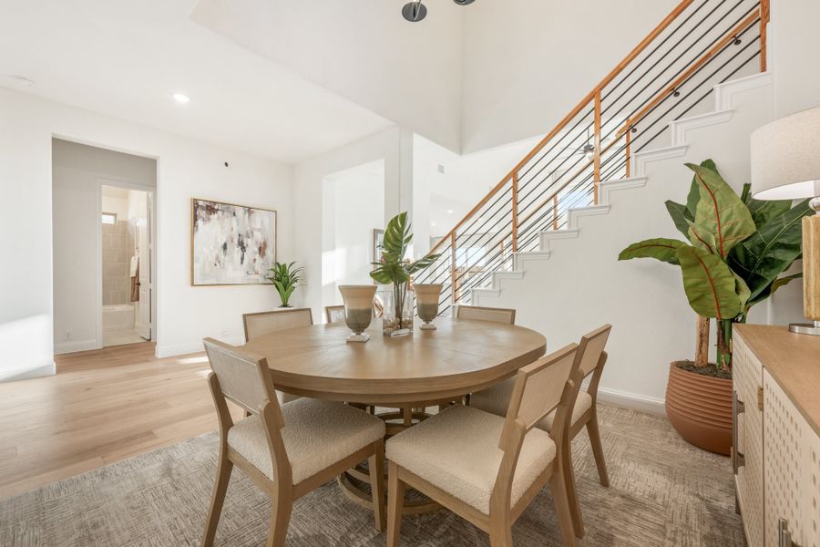 Dining room with round wood table, six chairs, high ceilings, and staircase with metal railing nearby
