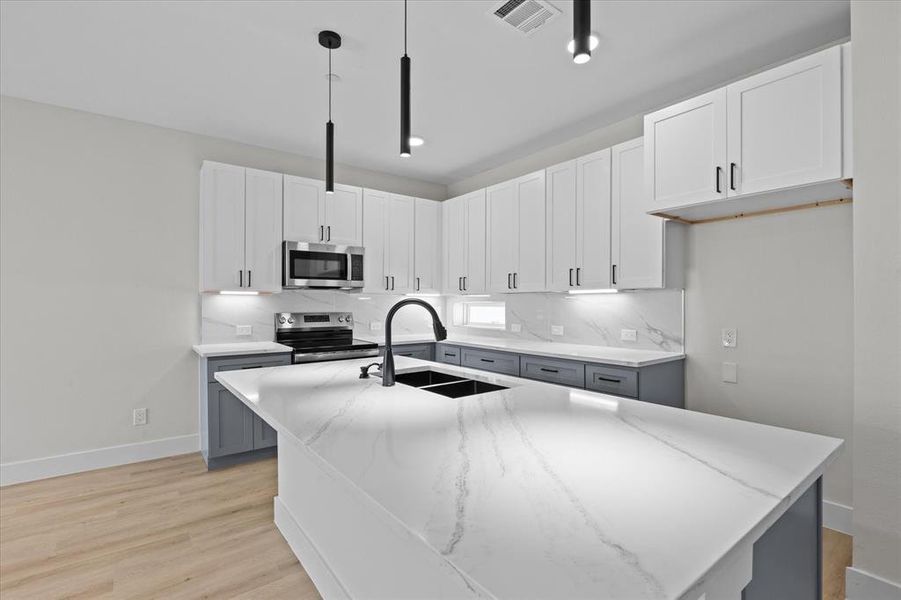 Kitchen with tasteful backsplash, light stone counters, appliances with stainless steel finishes, decorative light fixtures, and light wood-type flooring