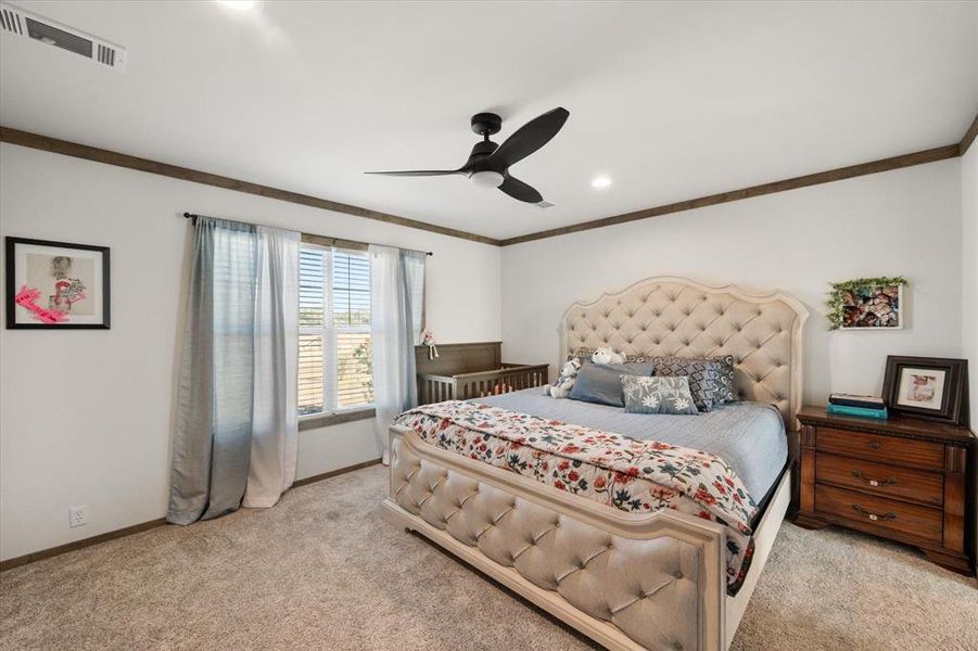 Carpeted bedroom featuring a large window with white blinds, wood-finish crown molding, a ceiling fan, and recessed lighting