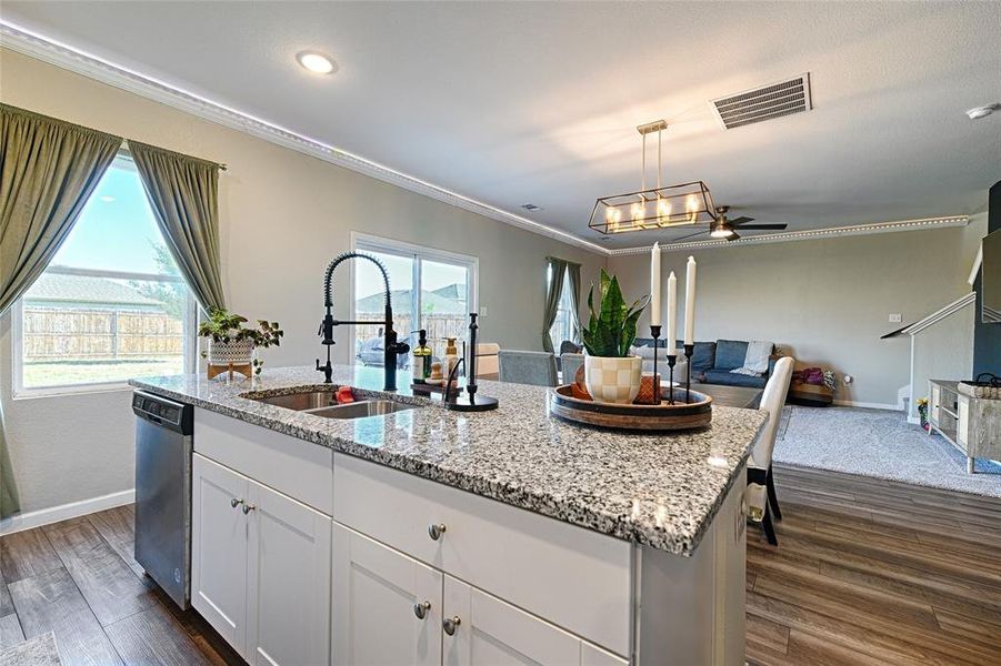 Kitchen featuring white cabinetry, open floor plan, a ceiling fan, light stone counters, and crown molding Kitchen featuring white cabinetry, open floor plan, a ceiling fan, light stone counters, and crown molding