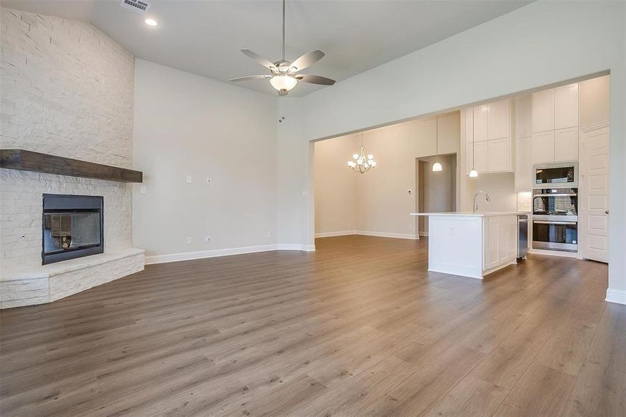 Unfurnished living room featuring a fireplace, ceiling fan with notable chandelier, hardwood / wood-style flooring, and sink