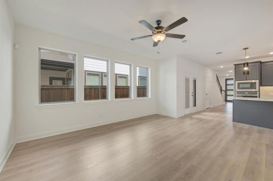 Open-concept living space with wood-finish flooring, a contemporary ceiling fan, and multiple windows