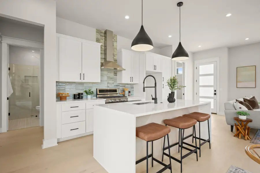 Kitchen featuring backsplash, white cabinets, light stone counters, a breakfast bar, and decorative light fixtures
