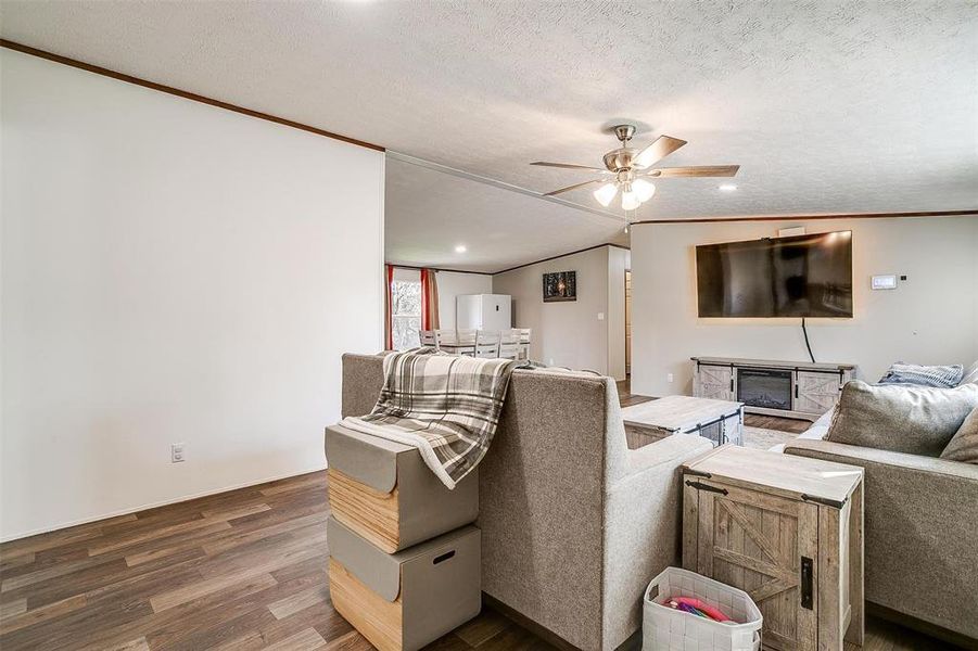 Living room featuring lofted ceiling, ceiling fan, crown molding, hardwood / wood-style flooring, and a textured ceiling