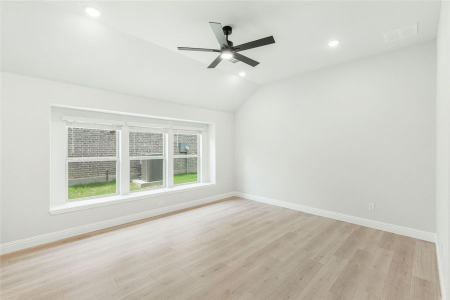 Empty room with vaulted ceiling, black ceiling fan, light wood floors, and large window