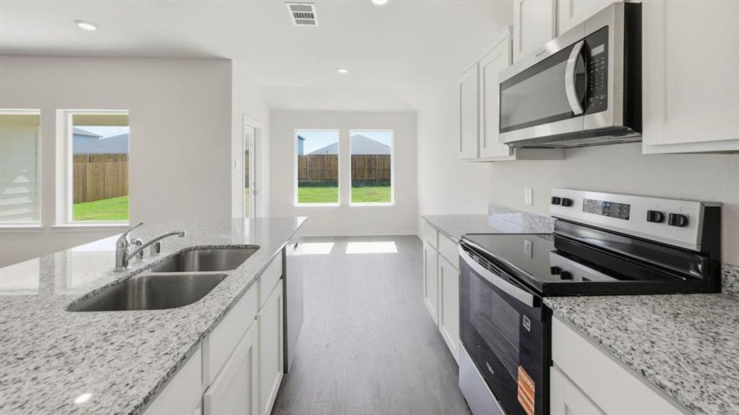 Kitchen with appliances with stainless steel finishes, white cabinets, light stone countertops, dark wood-type flooring, and recessed lighting