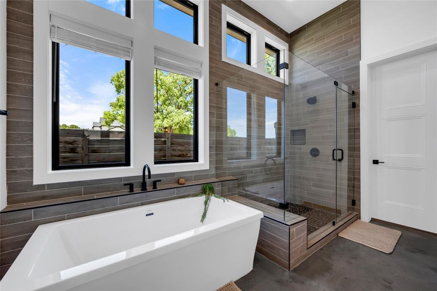 Contemporary bathroom featuring a freestanding soaking tub with matte black fixtures, a spacious walk-in shower with glass enclosure and pebble floor, and large windows with white blinds