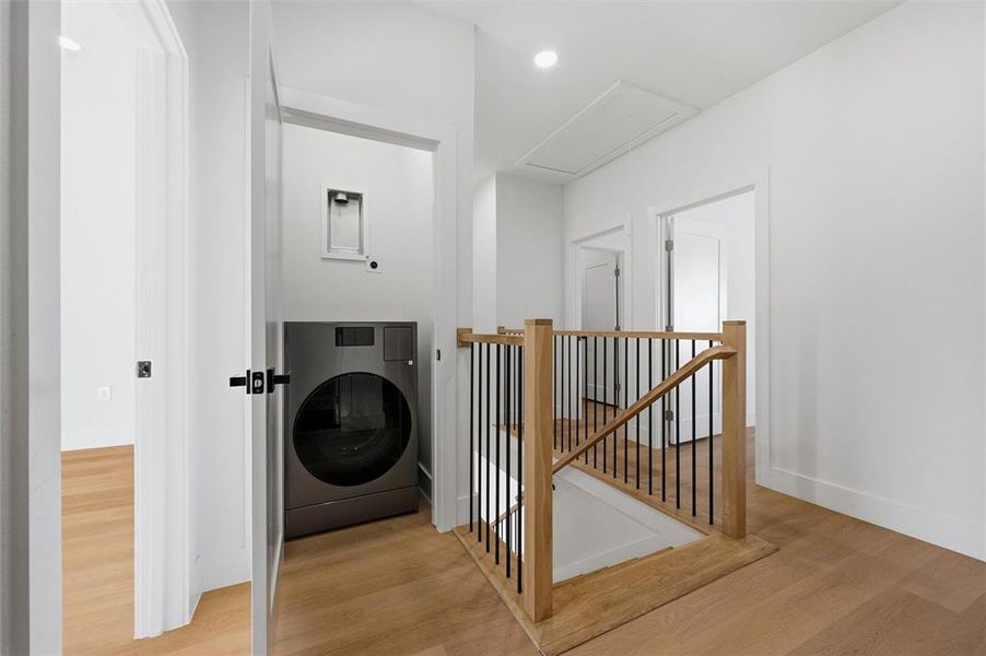 Utility Area features recessed lighting. Dedicated laundry area accommodates stacked washer and dryer connections. Adjacent staircase includes wood handrail with black metal balusters. Vinyl flooring extends throughout.