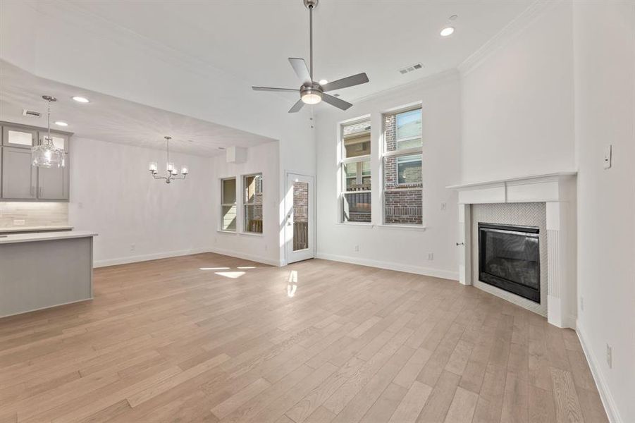 Unfurnished living room with ornamental molding, light hardwood / wood-style flooring, a tiled fireplace, and ceiling fan with notable chandelier