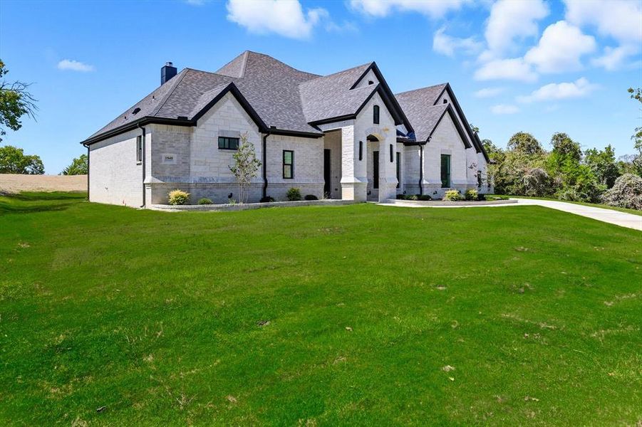 French country inspired facade with a front yard, stone siding, a chimney, and brick siding