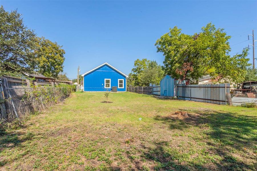 Spacious backyard featuring a blue exterior dwelling, mature trees, and a combination of chain-link and privacy fencing