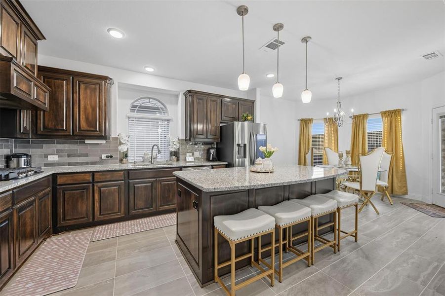 Kitchen featuring dark brown cabinets, a breakfast bar, a kitchen island, stainless steel appliances, and decorative backsplash Kitchen featuring dark brown cabinets, a breakfast bar, a kitchen island, stainless steel appliances, and decorative backsplash