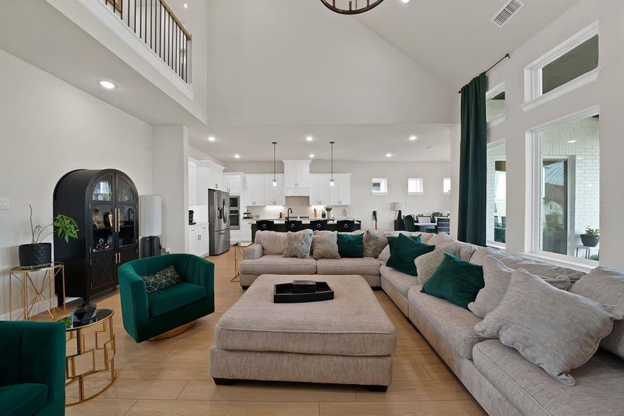 Open-concept living area featuring high vaulted ceilings, wood-finish flooring, and a second-story balcony overlook with black metal railings Open-concept living area featuring high vaulted ceilings, wood-finish flooring, and a second-story balcony overlook with black metal railings
