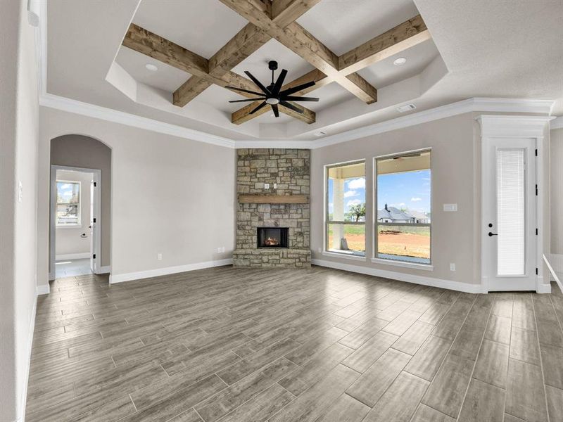 Unfurnished living room featuring coffered ceiling, baseboards, a ceiling fan, a stone fireplace, and wood tiled floor Unfurnished living room featuring coffered ceiling, baseboards, a ceiling fan, a stone fireplace, and wood tiled floor
