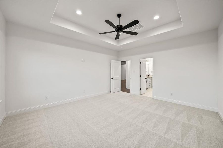 Unfurnished bedroom featuring a raised ceiling, light carpet, ceiling fan, and recessed lighting