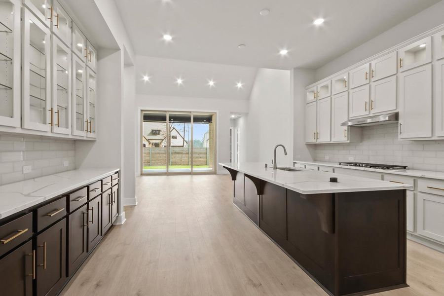 Kitchen with under cabinet range hood, white cabinetry, a sink, and light wood finished floors Kitchen with under cabinet range hood, white cabinetry, a sink, and light wood finished floors