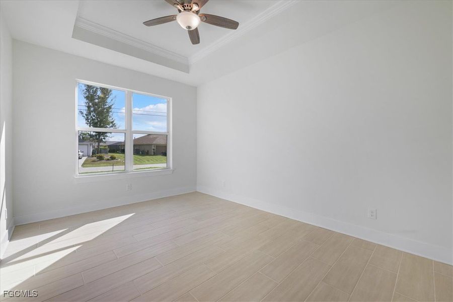 Empty room with a tray ceiling, wood tiled floors, ceiling fan, and crown molding