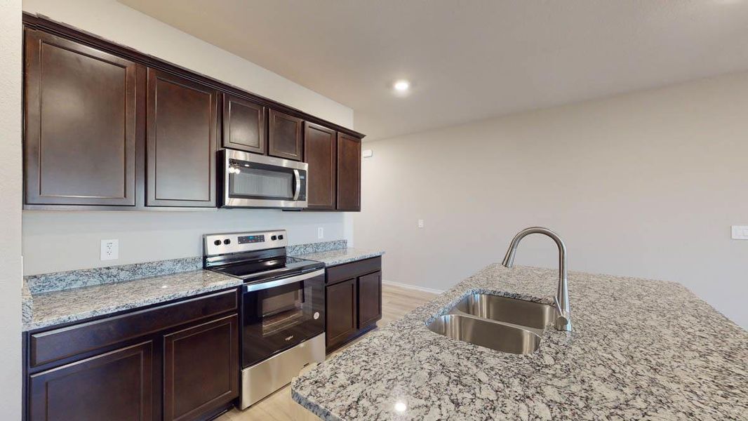 Kitchen featuring appliances with stainless steel finishes, light stone countertops, recessed lighting, dark brown cabinets, and a center island with sink