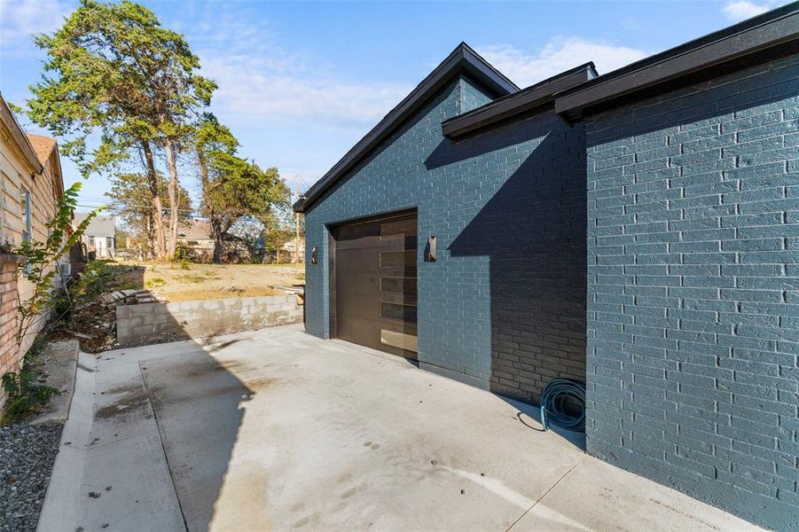View of side of property with brick siding, driveway, a patio, and an attached garage