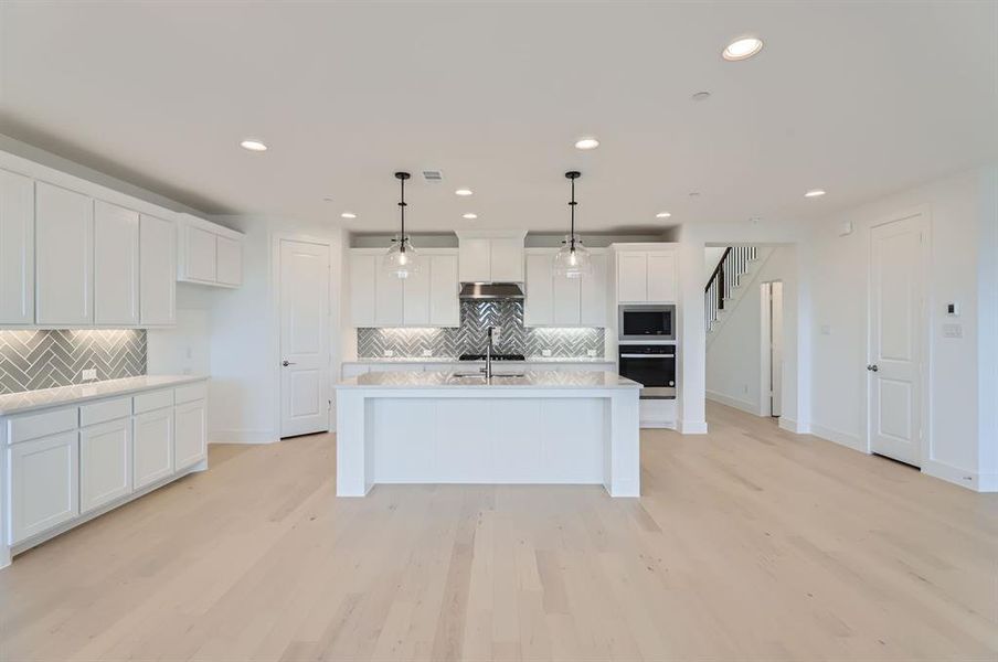 Kitchen featuring a kitchen island with sink, hanging light fixtures, stainless steel appliances, and light hardwood / wood-style flooring