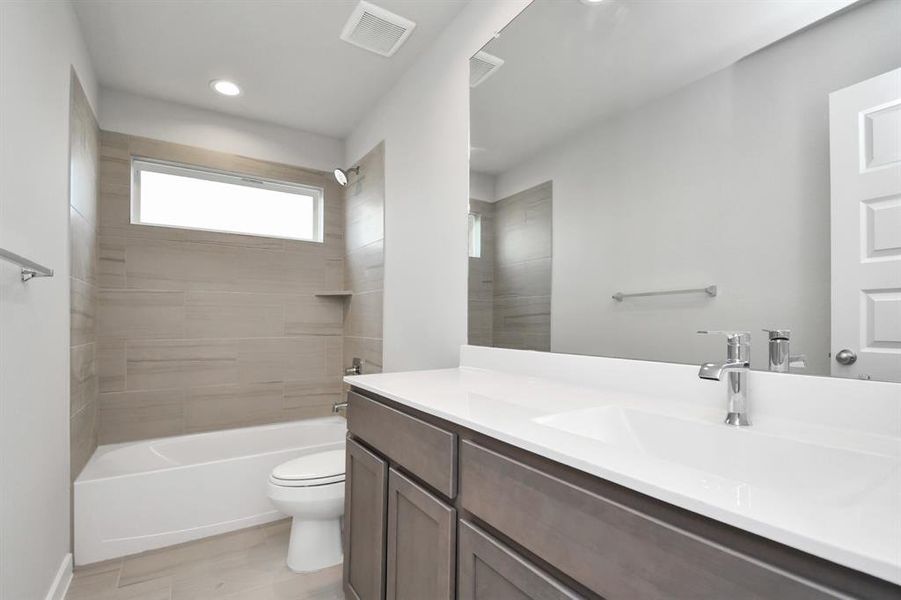 Experience sophistication in the secondary bathroom, where tile flooring complements a bath/shower combo with tile surround. Light wood cabinets complete with a beautiful light countertop, enhances the space for a truly inviting ambiance. Photo shown is example of completed home with similar plan. Actual colors and selections may vary.