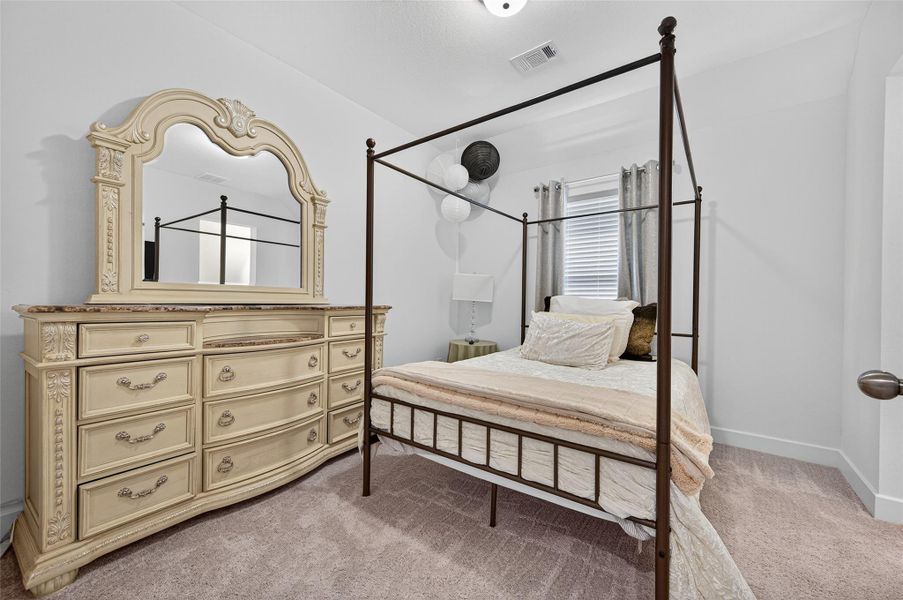 This bedroom features a stylish four-poster bed and an ornate dresser with a large mirror. It has neutral tones, carpeted flooring, and a window with curtains, creating a cozy and elegant atmosphere. This bedroom features a stylish four-poster bed and an ornate dresser with a large mirror. It has neutral tones, carpeted flooring, and a window with curtains, creating a cozy and elegant atmosphere.