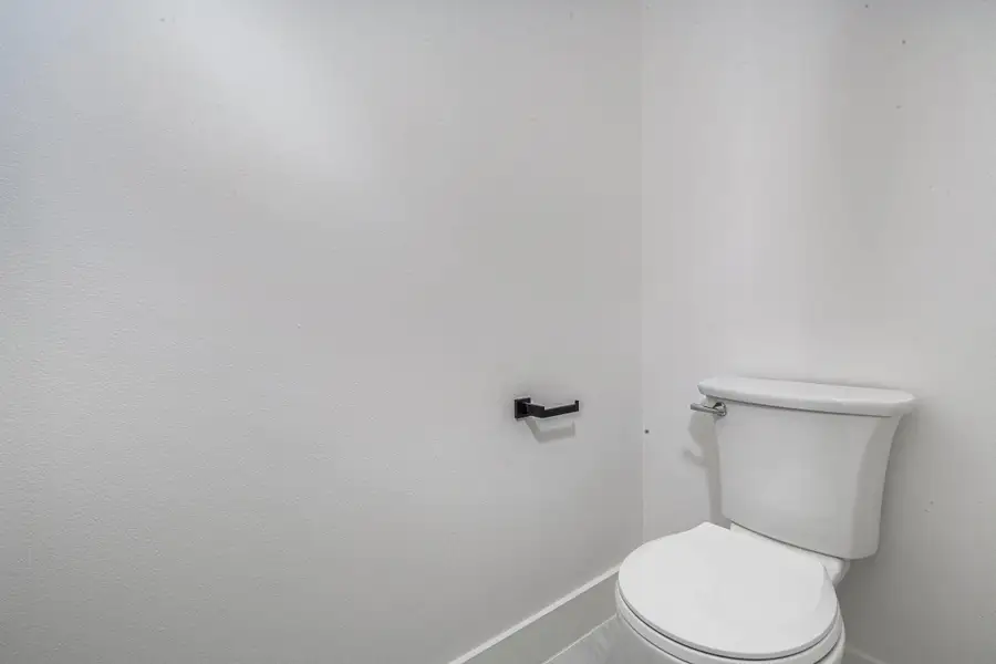 This is a minimalist, small bathroom with a white toilet and modern black toilet paper holder, featuring clean white walls and bright lighting.