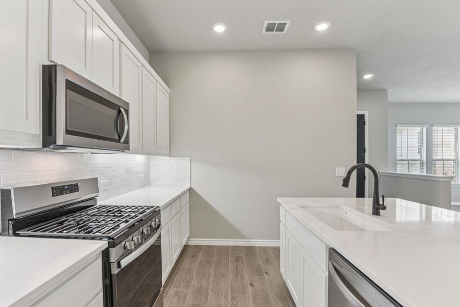 Kitchen with appliances with stainless steel finishes, white cabinetry, wood tiled floors, light stone countertops, and recessed lighting Kitchen with appliances with stainless steel finishes, white cabinetry, wood tiled floors, light stone countertops, and recessed lighting