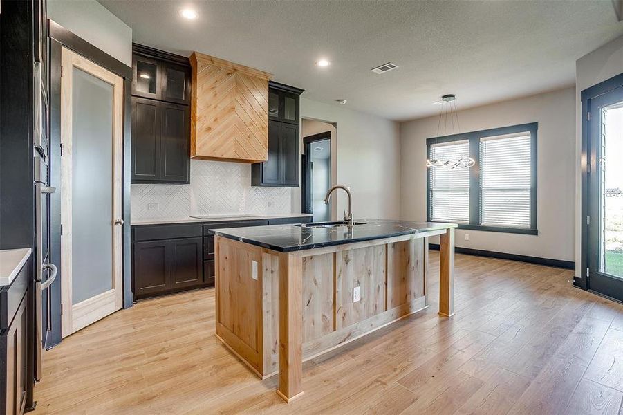 Kitchen with sink, a kitchen island with sink, decorative light fixtures, decorative backsplash, and light wood-type flooring