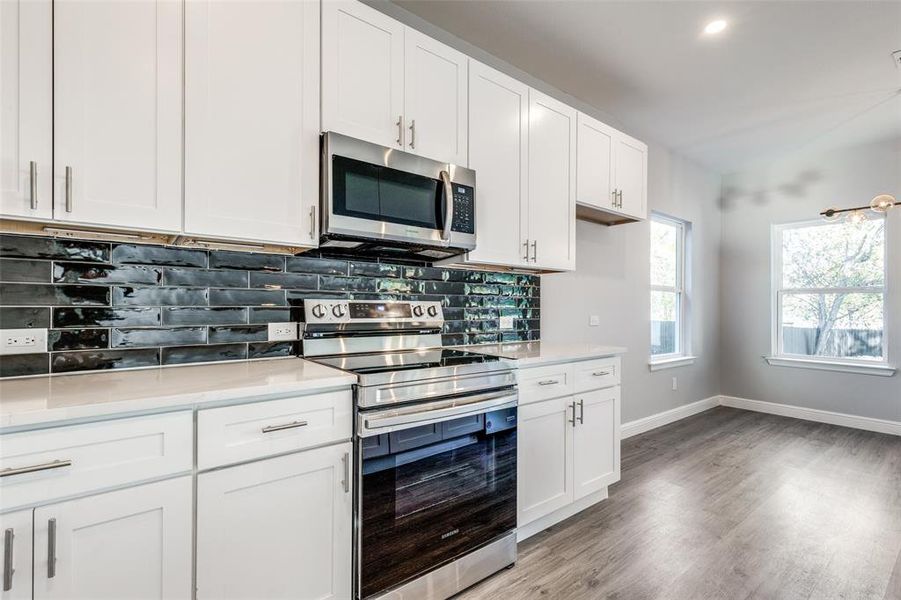 Kitchen with white cabinetry, appliances with stainless steel finishes, light hardwood / wood-style floors, and backsplash