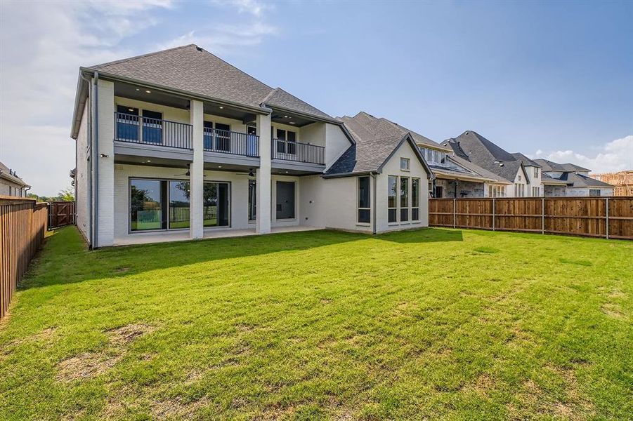 Back of property featuring a balcony, a fenced backyard, a shingled roof, a ceiling fan, and a patio Back of property featuring a balcony, a fenced backyard, a shingled roof, a ceiling fan, and a patio