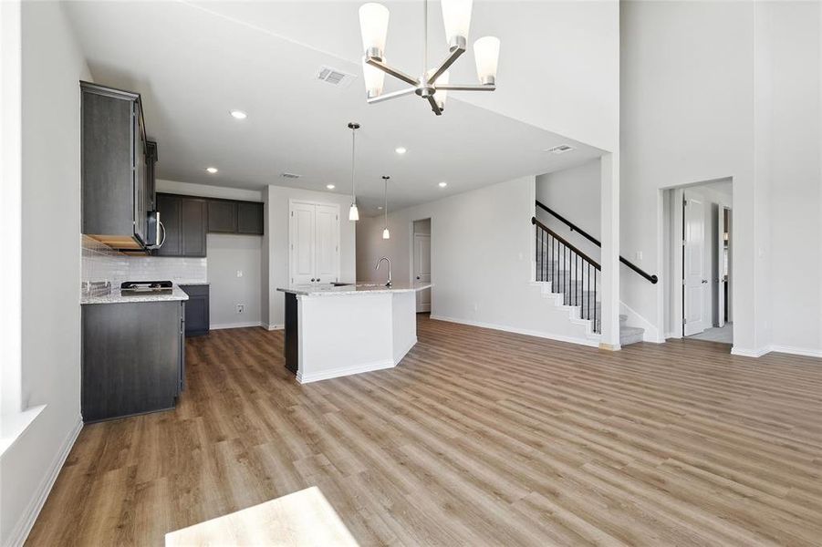 Kitchen featuring recessed lighting, a chandelier, light wood-type flooring, a center island with sink, and decorative light fixtures Kitchen featuring recessed lighting, a chandelier, light wood-type flooring, a center island with sink, and decorative light fixtures