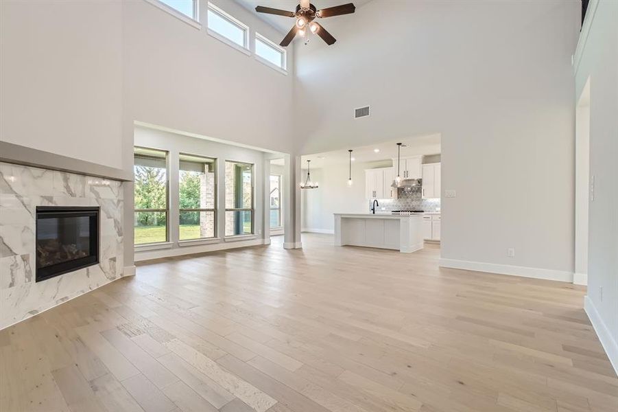 Unfurnished living room with light hardwood / wood-style floors, a high ceiling, a fireplace, and ceiling fan