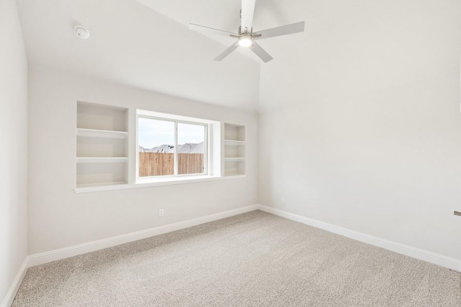 Empty bedroom with vaulted ceiling, ceiling fan, built-in shelves flanking a window, and carpet flooring