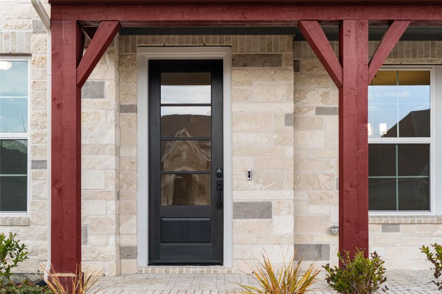 This covered front porch makes a grand first impression, showcasing a sophisticated blend of natural stone veneer and bold, dark-stained timber beams. The entryway is anchored by a stately black-framed glass front door, creating a modern yet warm transition into this stunning home. This covered front porch makes a grand first impression, showcasing a sophisticated blend of natural stone veneer and bold, dark-stained timber beams. The entryway is anchored by a stately black-framed glass front door, creating a modern yet warm transition into this stunning home.
