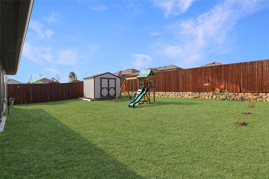 Fenced backyard featuring a storage shed and a playground