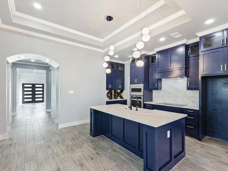 Kitchen with glass fronted cabinets, arched walkways, light stone counters, a kitchen island with sink, and pendant lighting Kitchen with glass fronted cabinets, arched walkways, light stone counters, a kitchen island with sink, and pendant lighting
