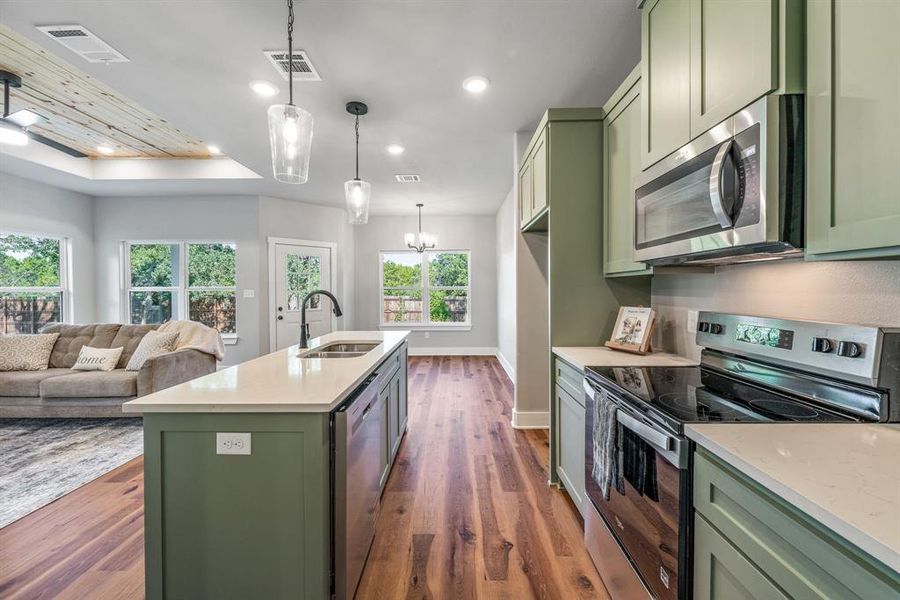 Kitchen with green cabinetry, stainless steel appliances, dark wood finished floors, light stone countertops, and pendant lighting Kitchen with green cabinetry, stainless steel appliances, dark wood finished floors, light stone countertops, and pendant lighting