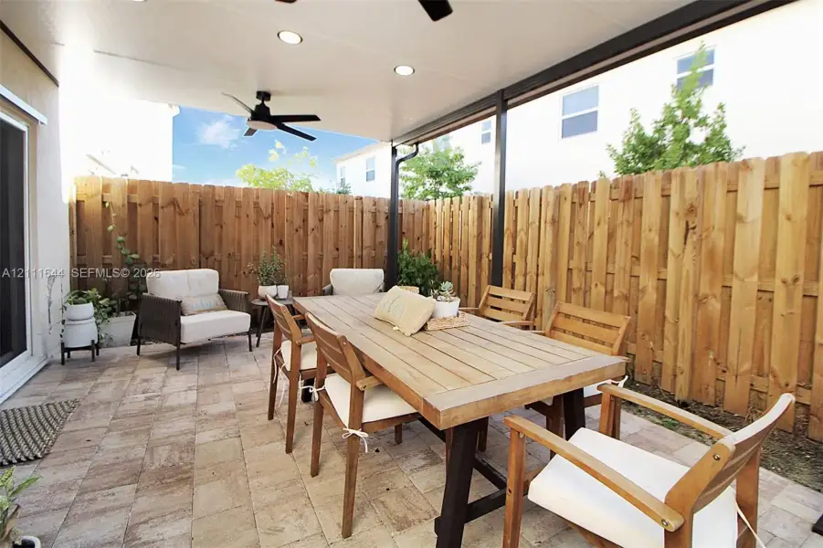 Covered patio featuring paver flooring, a wooden perimeter privacy fence, and a mounted ceiling fan with integrated lighting Covered patio featuring paver flooring, a wooden perimeter privacy fence, and a mounted ceiling fan with integrated lighting