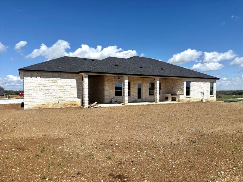 Rear view of property featuring a patio, stone siding, and a shingled roof