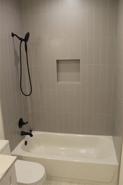 A sleek, contemporary bathroom features a pristine white bathtub and dark bronze fixtures against tiled walls.